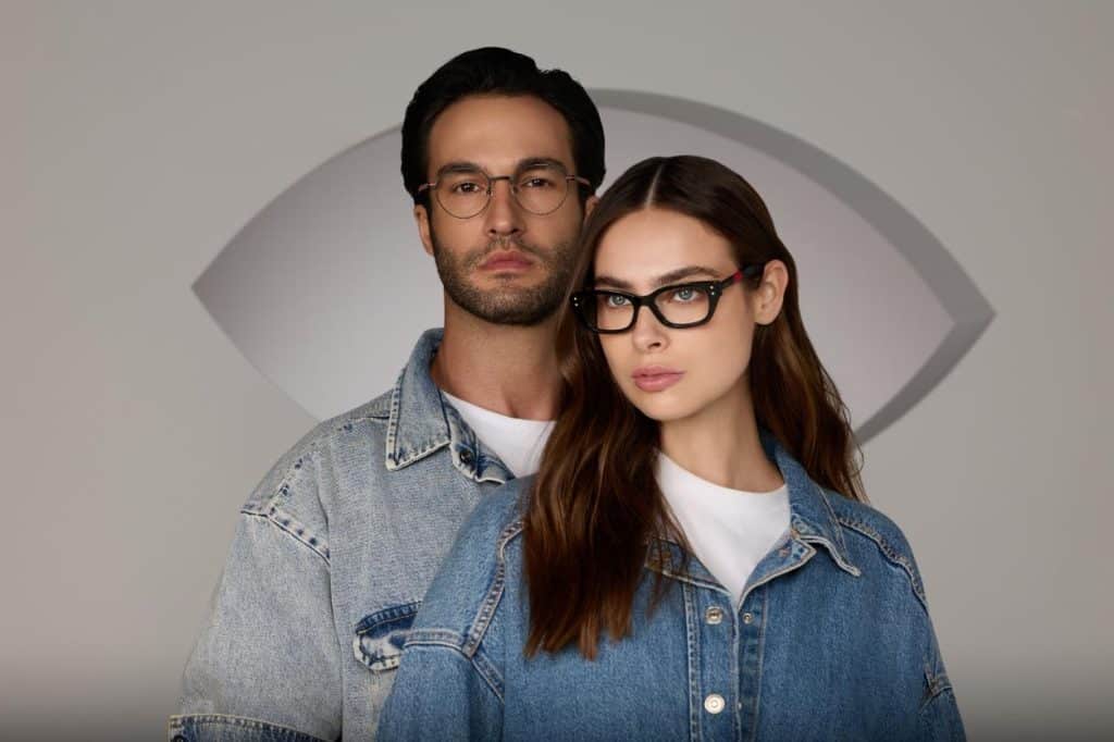 גבר ואישה עם משקפיים ומעילים ג'ינס מצטלמים על רקע בצורת עין, במטרה להעלות את המודעות לבריאות העיניים.